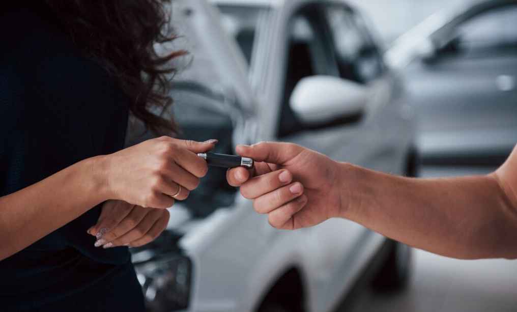 A man handing over car keys to another person with a stack of money in exchange