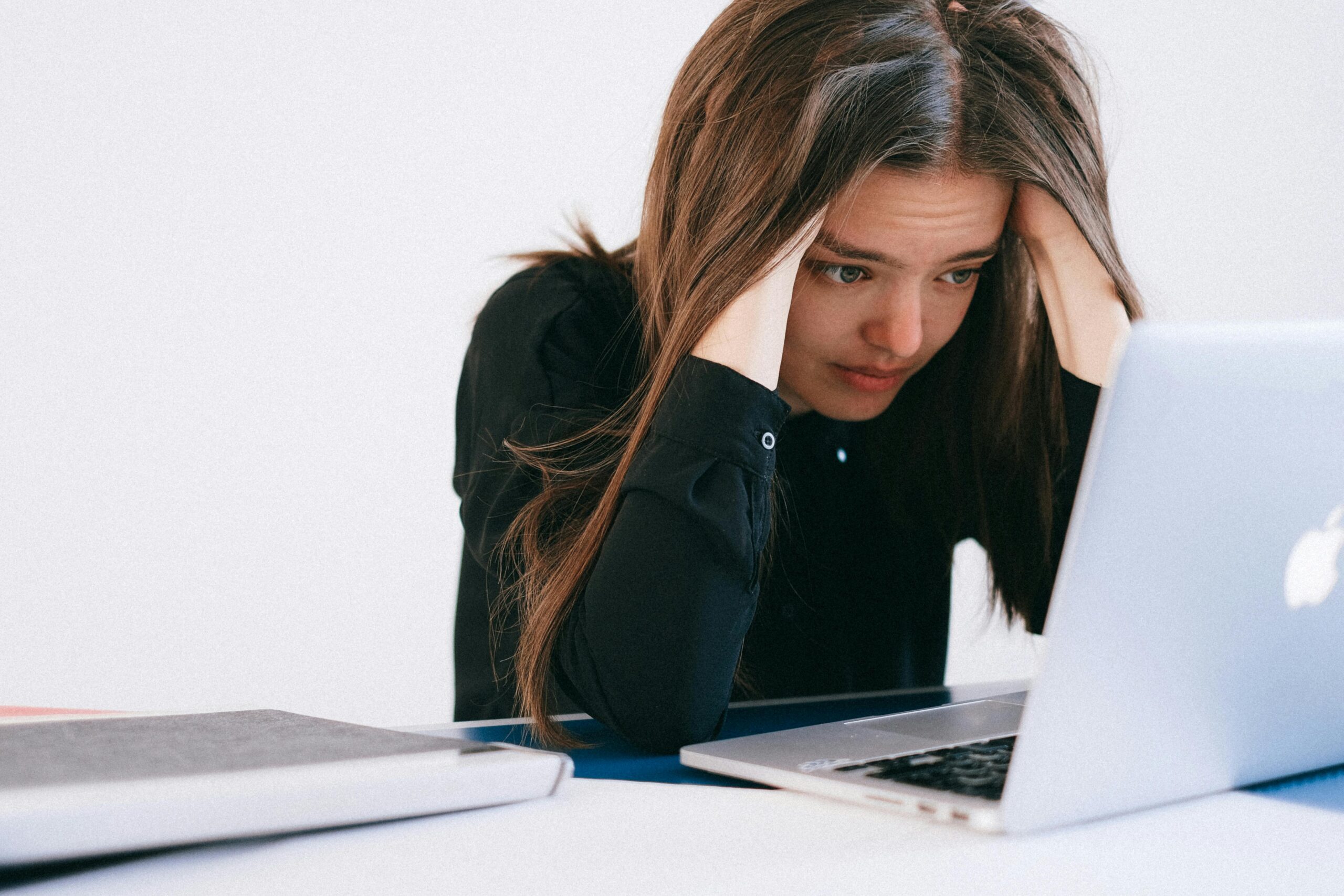 The image shows a young woman sitting at a desk, looking stressed or frustrated as she stares at her laptop screen