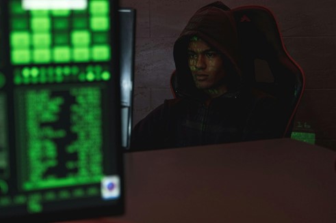 a man with a hood is sitting in the dark looking at a computer screen