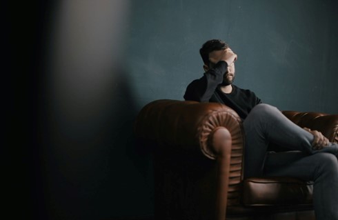 A worried man sitting on a sofa with his hand on his face