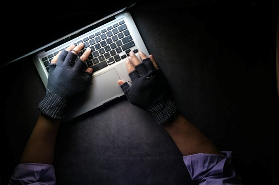 Person in gloves typing on a laptop, possibly engaging in a deepfake scam