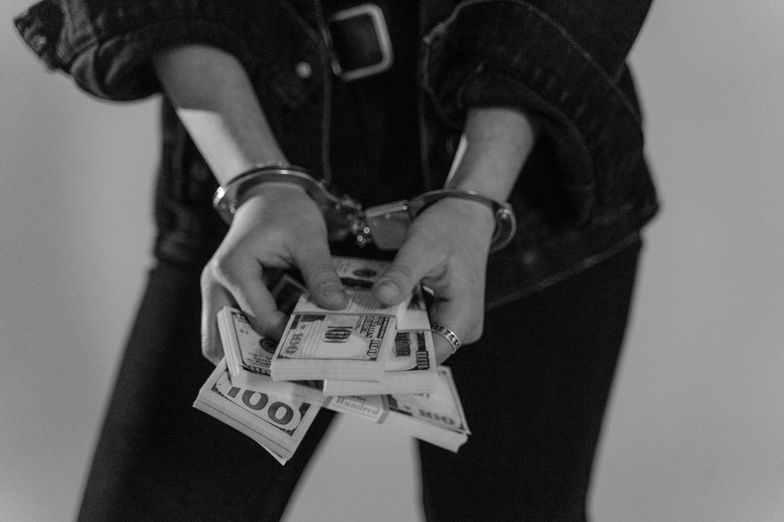 Hands holding dollar bills and with handcuffs