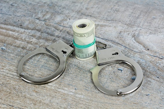 Handcuffs and a roll of U.S. dollars on a textured surface, symbolizing financial crime