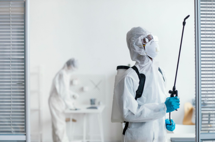 Two pest control workers in protective suits spraying office