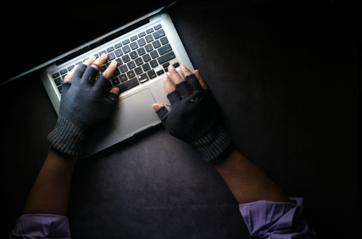 Person wearing gloves typing on a laptop in a dark setting