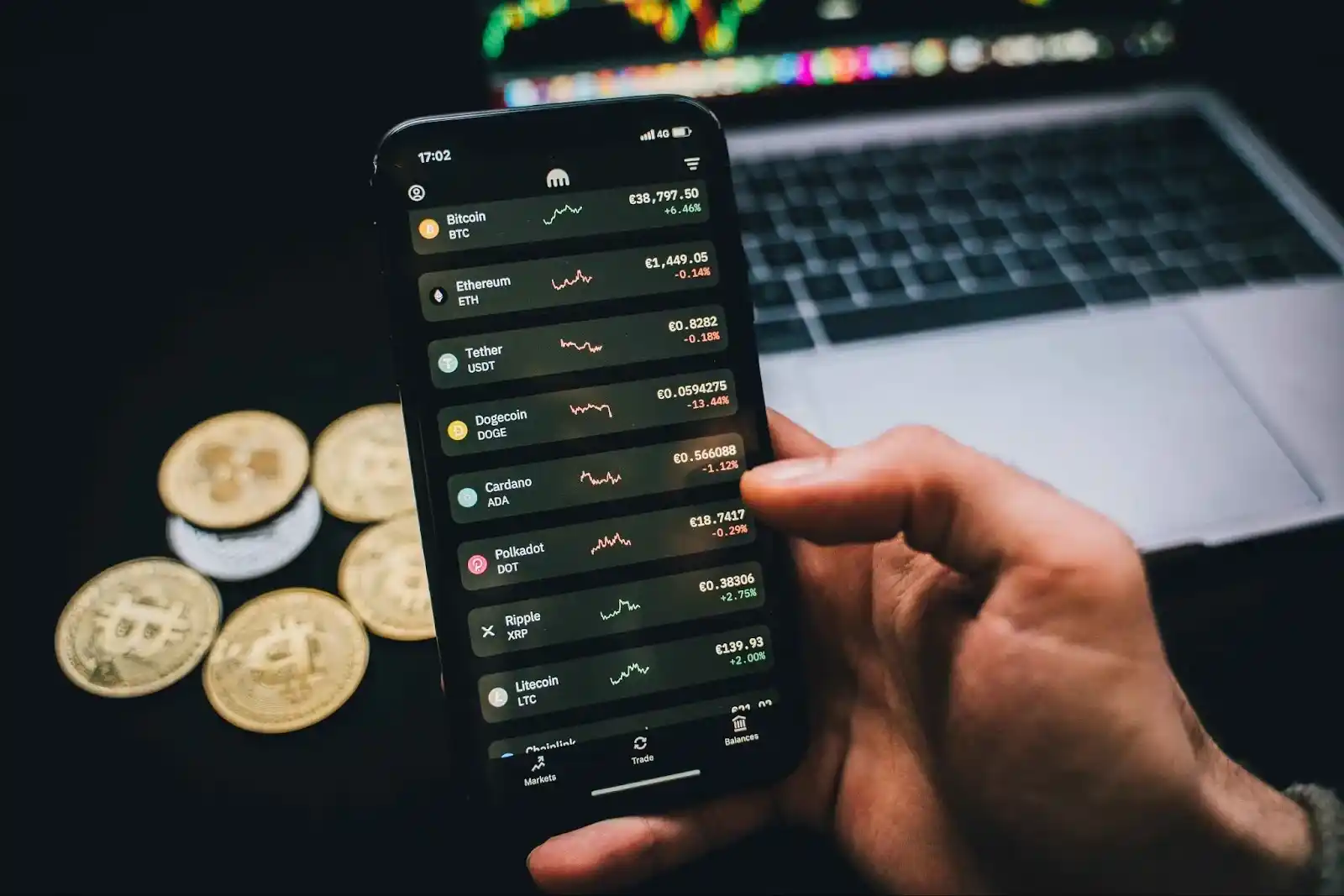 Person holding a phone showing cryptocurrency prices with Bitcoin coins nearby