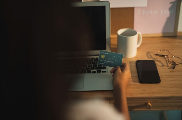 Person holding a credit card in front of a laptop in a dimly lit setting