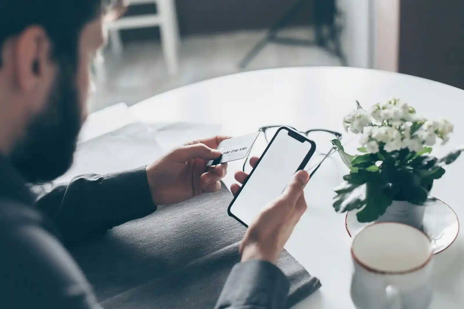 Man holding a credit card and a mobile phone, representing the risk of online scams and financial fraud