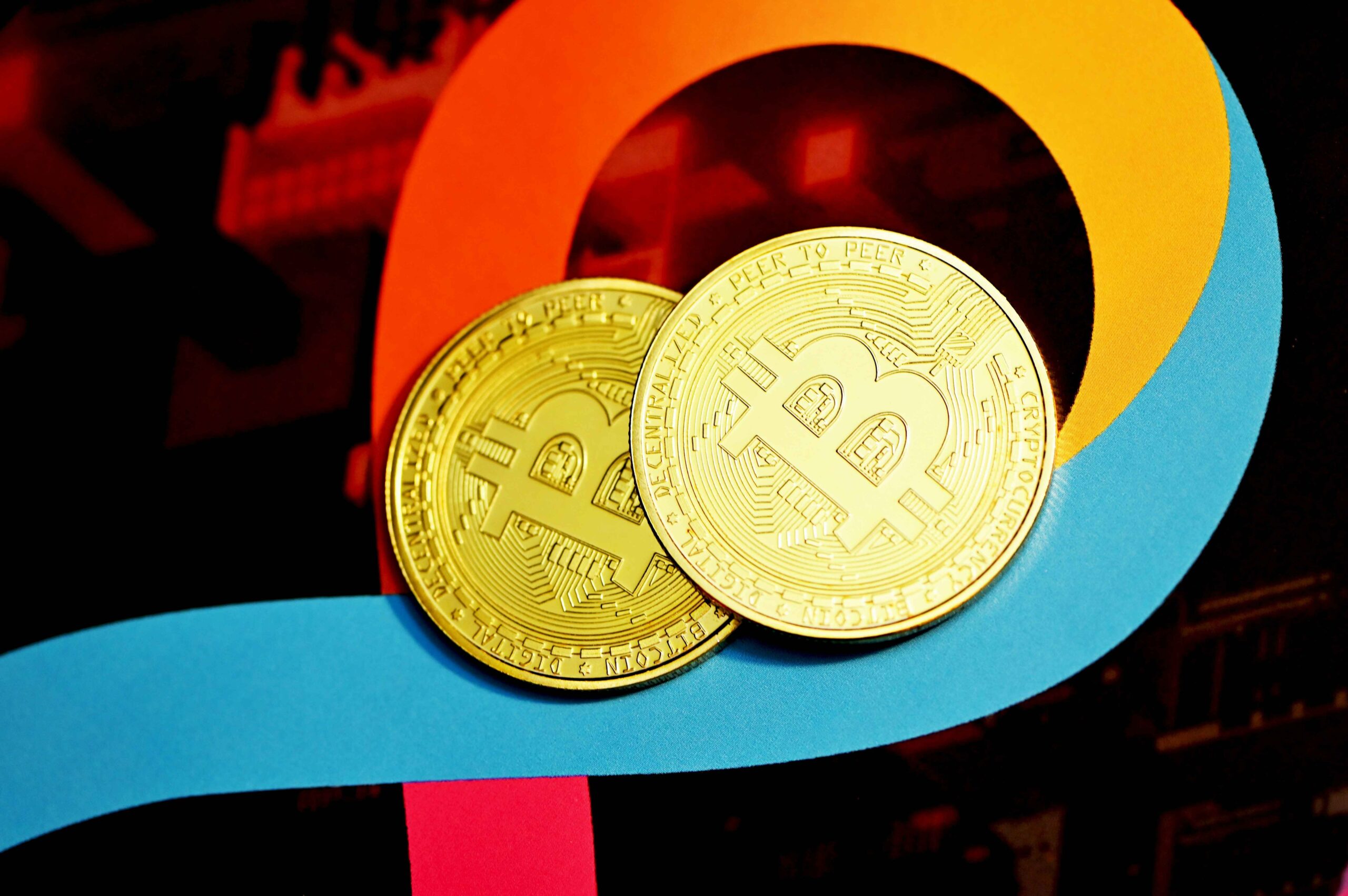 Two gold Bitcoin coins placed on a colorful abstract background, representing cryptocurrency and digital finance concepts