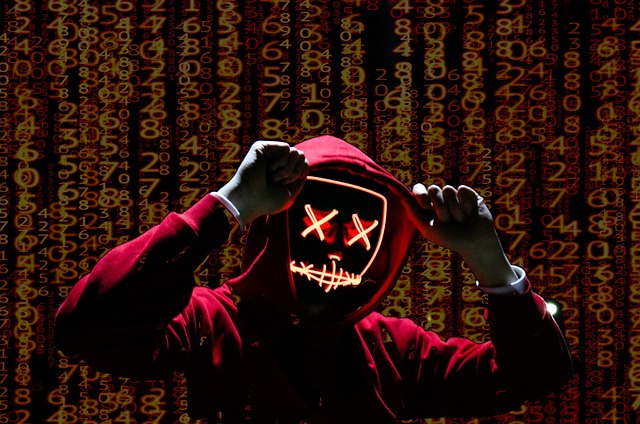 Person in a red hoodie wearing an LED hacker mask, with digital numbers in the background representing cyber threats