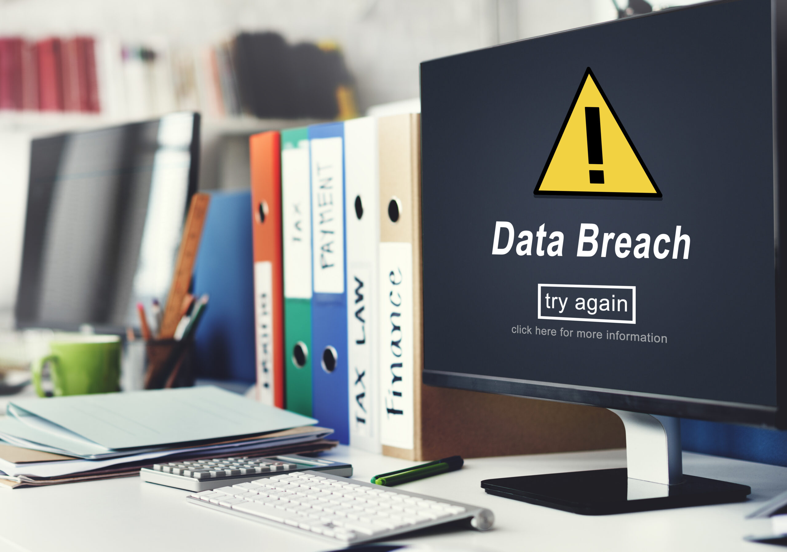Warning sign on computer showing Data Breach Alert message in an office environment with files and documents