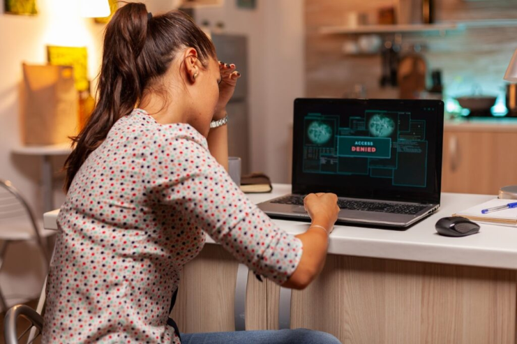 Upset woman using laptop with access denied warning on screen in home office